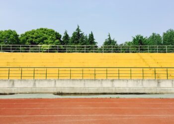 Açık havada sarı tribünler ve önünde kırmızı koşu parkuru olan bir stadyum.