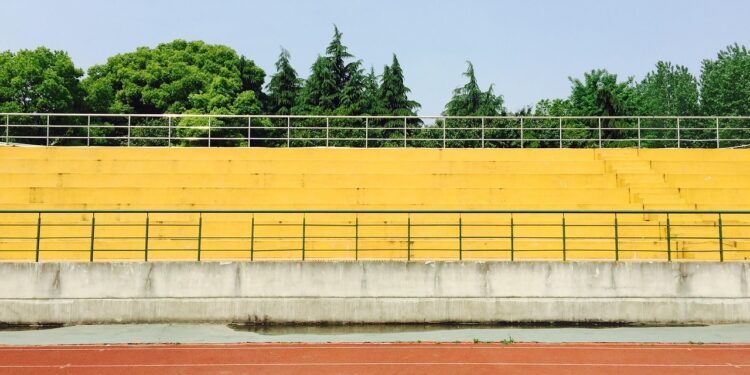 Açık havada sarı tribünler ve önünde kırmızı koşu parkuru olan bir stadyum.