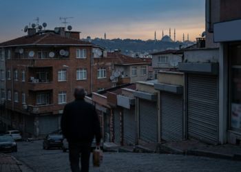 Alacakaranlıkta sokakta yürüyen bir kişi ve arka planda silueti görünen tarihi şehir.