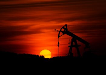 Kızıl gün batımında silüet halinde çalışan bir petrol sondaj kulesi.