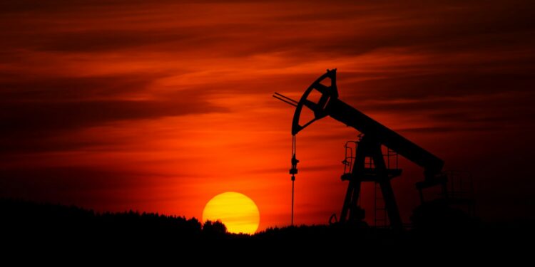 Kızıl gün batımında silüet halinde çalışan bir petrol sondaj kulesi.