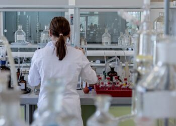 Laboratuvarda çalışan, önlük giymiş saçını toplamış kadın araştırmacı.