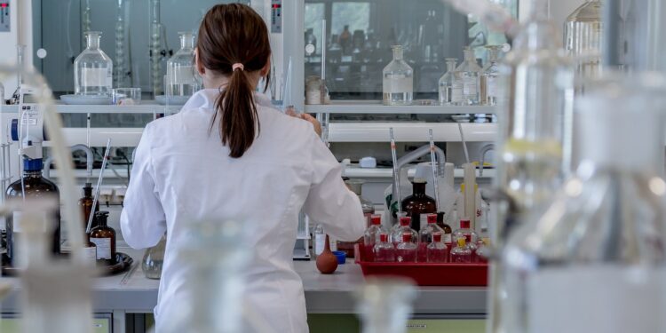 Laboratuvarda çalışan, önlük giymiş saçını toplamış kadın araştırmacı.