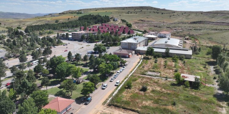 Ağaçlar, yapılar ve binalarla çevrili geniş bir yerleşim alanının havadan görünümü.
