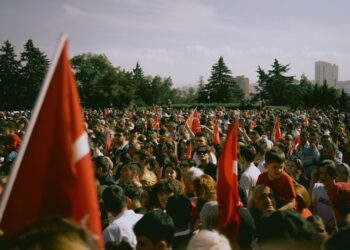 Açık havada ellerinde Türk bayrakları sallayan kalabalık bir kalabalık grup insan.