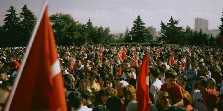 Açık havada ellerinde Türk bayrakları sallayan kalabalık bir kalabalık grup insan.
