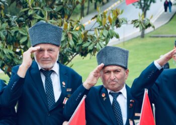 Geleneksel kıyafetler giymiş ve törende selam duran yaşlı gaziler.
