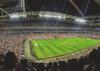 Geniş açıyla çekilmiş gece stadyumunda oynanan futbol maçı ve kalabalık tribünler.