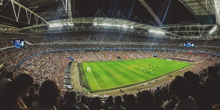 Geniş açıyla çekilmiş gece stadyumunda oynanan futbol maçı ve kalabalık tribünler.