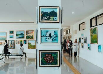 Sanat galerisinde duvardaki tabloları inceleyen insanlar ve sütundaki tablolar