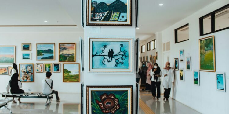 Sanat galerisinde duvardaki tabloları inceleyen insanlar ve sütundaki tablolar