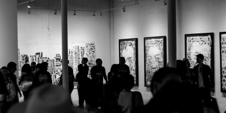 Siyah beyaz fotoğrafta sanat galerisindeki tablo ve eserleri inceleyen kalabalık.
