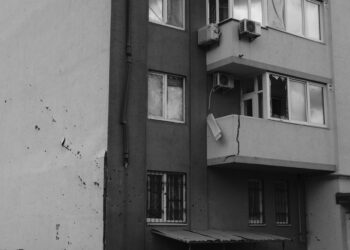 Hasar almış balkonu ve duvarında çatlaklar bulunan gri bir apartman binası.