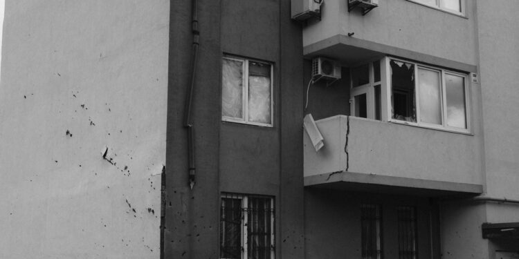 Hasar almış balkonu ve duvarında çatlaklar bulunan gri bir apartman binası.