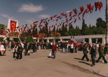 Açık havada düzenlenen bir festival alanında kalabalık insanlar ve asılı bayraklar.