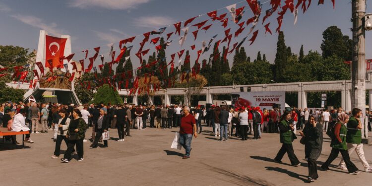 Açık havada düzenlenen bir festival alanında kalabalık insanlar ve asılı bayraklar.