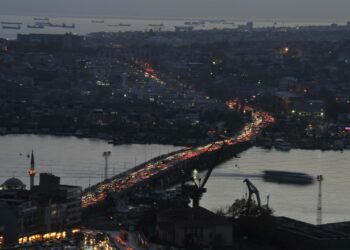 Karanlıkta kıvrılarak uzanan bir köprü üzerinde yoğun trafik ve ışıklar.