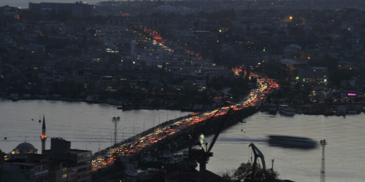 Karanlıkta kıvrılarak uzanan bir köprü üzerinde yoğun trafik ve ışıklar.