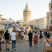 Tarihi sokakta yer alan modern sanat yerleştirmesini inceleyen kalabalık festival ziyaretçileri.