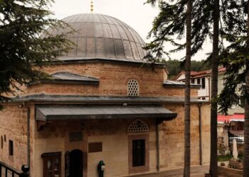 Tarihi taş duvarlı ve kurşun kubbeli Osmanlı dönemi cami ve çevresindeki çam ağaçları.