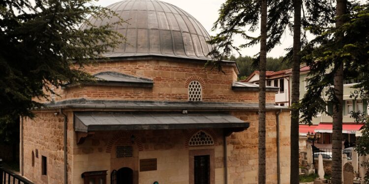 Tarihi taş duvarlı ve kurşun kubbeli Osmanlı dönemi cami ve çevresindeki çam ağaçları.