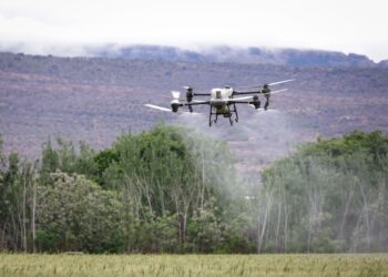 Tarlalara ilaçlama yapan modern tarım dronu ve arka planda dağ manzarası