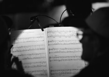 Aydınlatılmış nota sehpası üzerinde klasik müzik notaları ve arkada insan silüetleri