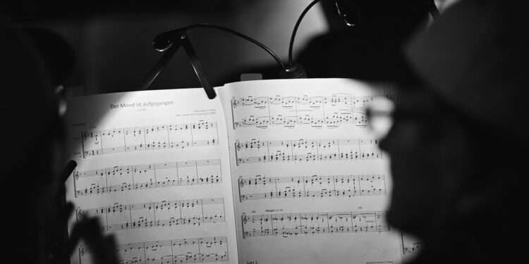 Aydınlatılmış nota sehpası üzerinde klasik müzik notaları ve arkada insan silüetleri