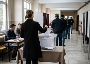Bir okul koridorunda sandık başına gidip oy kullanan insanlar.
