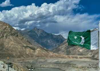 Dağlar ve bulutlu gökyüzü önünde dalgalanan Pakistan bayrağı.