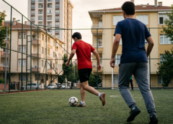 Sokak aralarındaki halı sahasında futbol oynayan gençlerin neşeli mücadelesi.