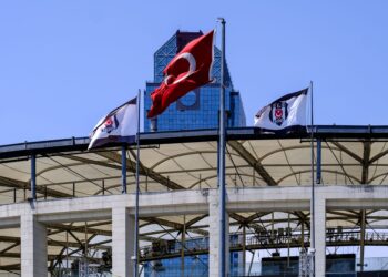 Stadyumda dalgalanan Türk bayrağı ve arka planda modern bir bina.
