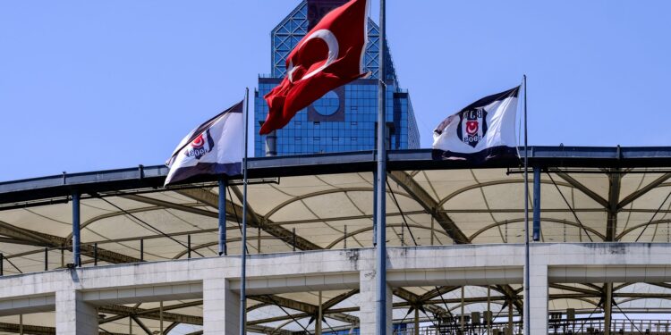 Stadyumda dalgalanan Türk bayrağı ve arka planda modern bir bina.