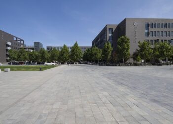 Geniş bir meydan, arka planda modern binalar ve ağaçlar.