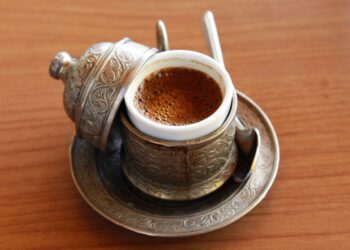 Ahşap masa üzerinde geleneksel fincanda köpüklü Türk kahvesi duruyor.
