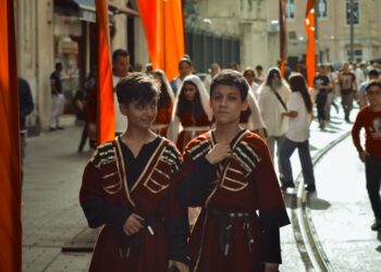 Geleneksel kıyafetler giymiş iki çocuk sokakta yürürken görülüyor.